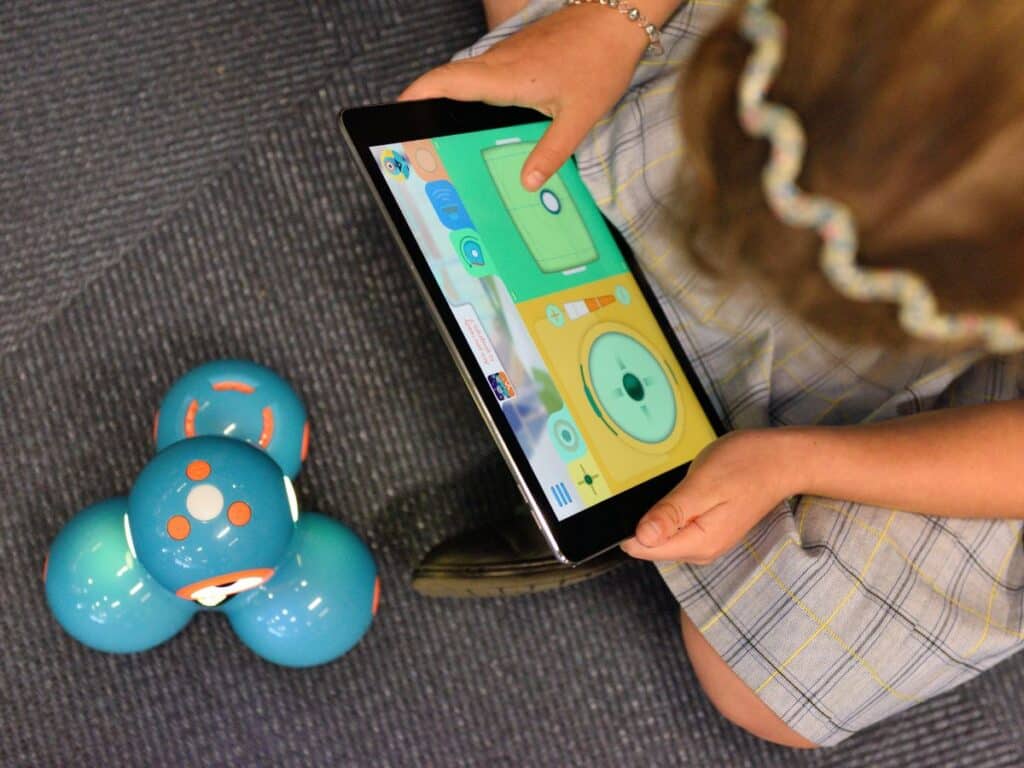 A top-down view of a kid using a tablet to code a robot