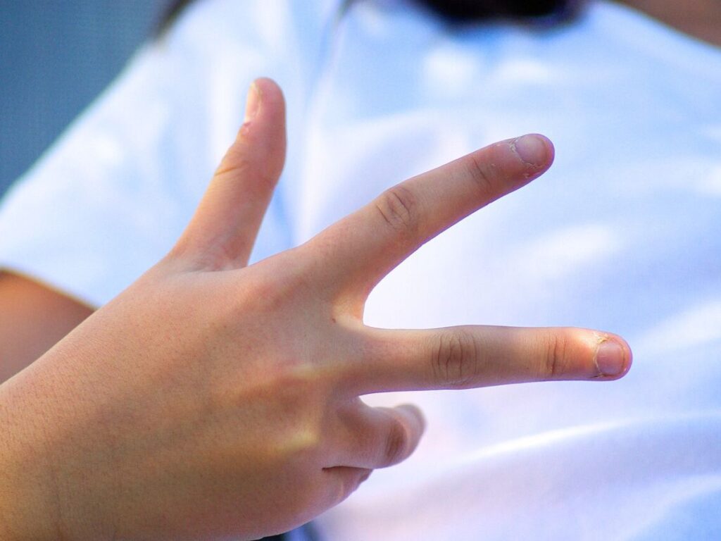 A child holding up 3 fingers to practice counting phonemes in words.